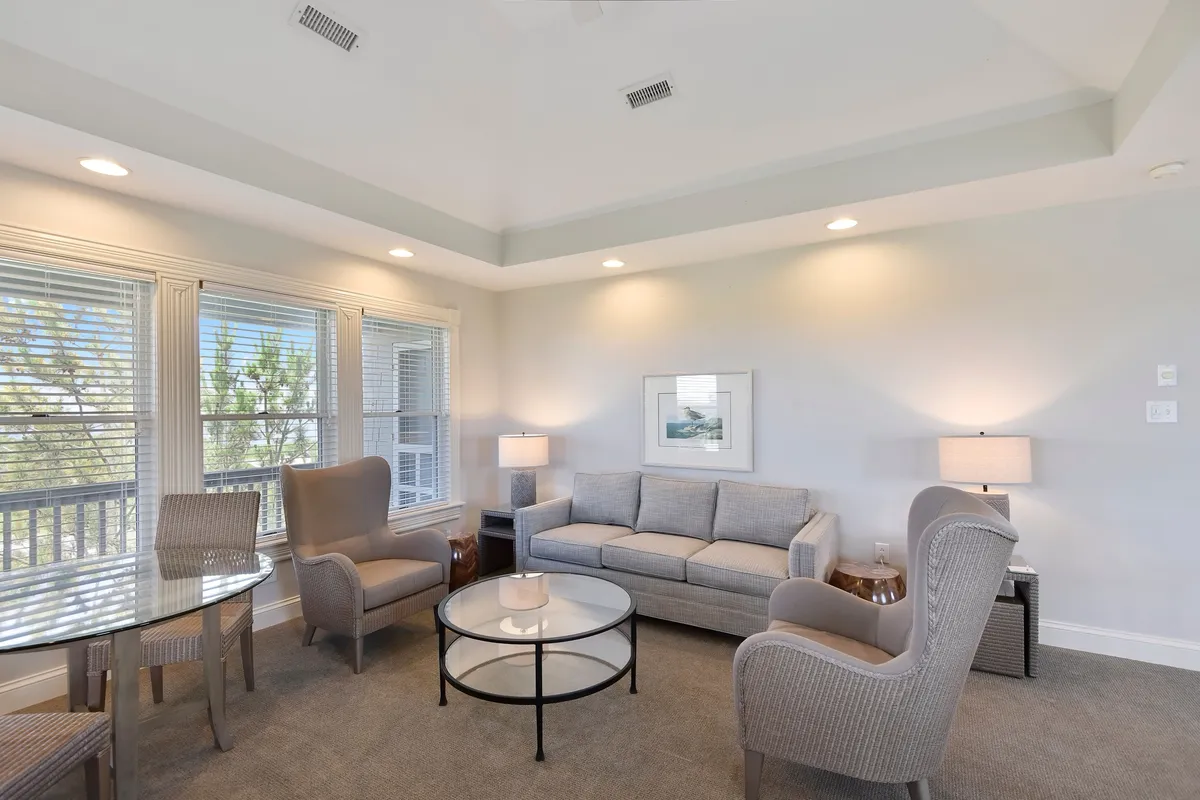 A sunlit room featuring a sofa, armchairs, and a coffee table set against windows that allow natural light to pour in. The arrangement is perfect for intimate family moments, reading, or casual conversation, evoking a sense of warmth and tranquility.