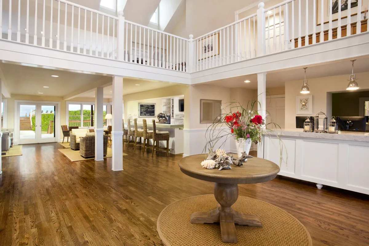 A central round dining table with a vibrant floral arrangement sits adjacent to an open kitchen, with large windows looking out to the outdoors. The scene feels cheerful and ready for entertaining, blending indoor comfort with views of nature.