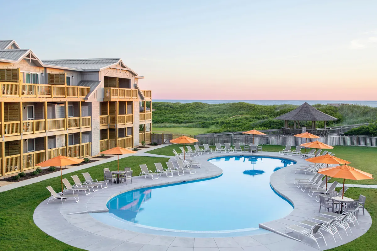 A welcoming pool area with lounge chairs, umbrellas, and a view of the building exterior and landscaped grounds. The setting is perfect for swimming, sunbathing, and socializing, with the potential for relaxing poolside gatherings under the sun or stars.