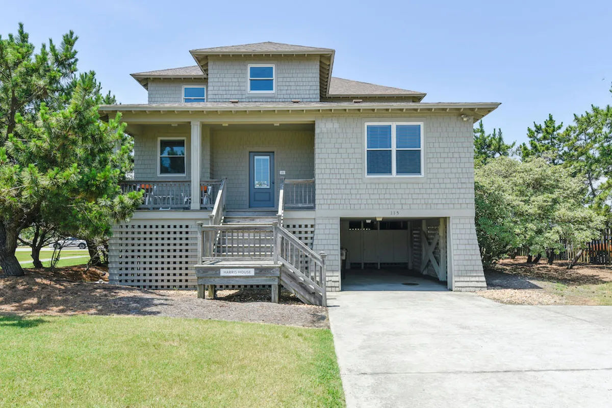 An inviting front porch with a staircase, large windows, and lush landscaping. The space is styled for outdoor gatherings, with ample room for family barbecues, morning coffees, or evening get-togethers. The expansive porch overlooks scenic surroundings, setting the tone for a welcoming home base.