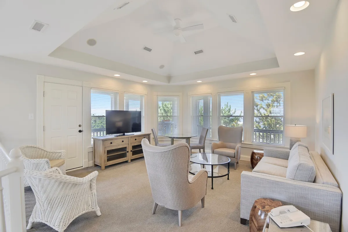 A comfortable seating area with a large window, cozy couches, a coffee table, and a television. The space feels calm and welcoming, with soft lighting and the promise of sunset views through the windows, suggesting an ideal spot for relaxation and group activities.